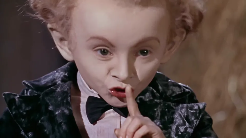Rumpelstiltskin AI clip still: the dancer raises a finger to his lips and grins at the camera in the hay barn